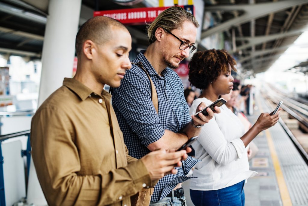 Three people texting on their phone at train station