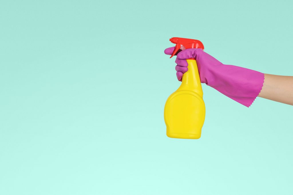Hand in rubber glove holding spray bottle of cleaning liquid
