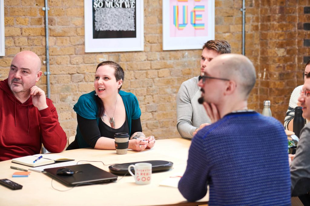 People in a stylish office sitting around a desk, looking at a screen out of shot