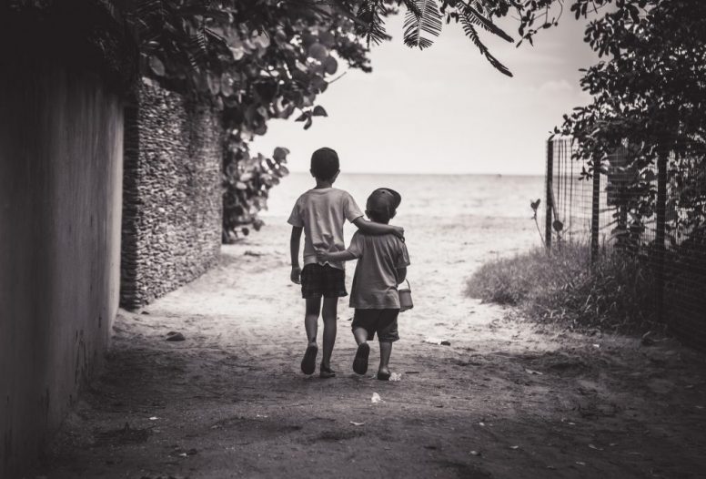 Two young boys wearing caps walking with arms around each other