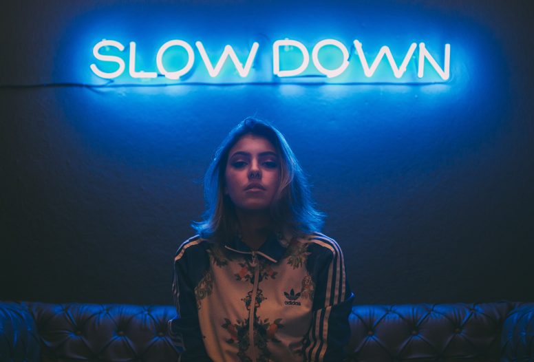 Woman standing in front of neon light that reads slow down