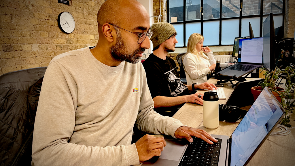Image of Ash Matadeen working at a laptop with colleagues in the background