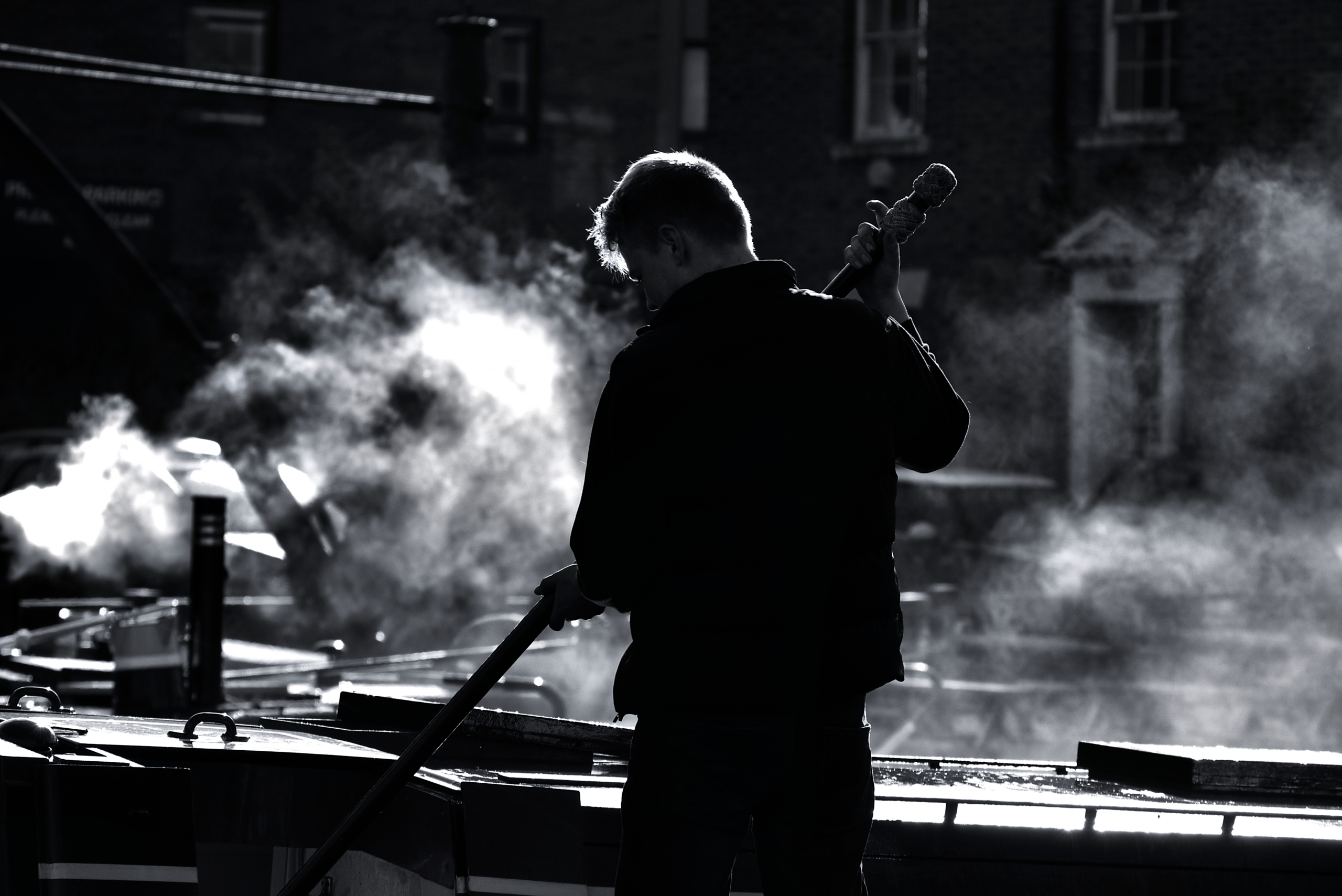 Narrowboat crew member handling a pole amid steam, on a historic working canal boat